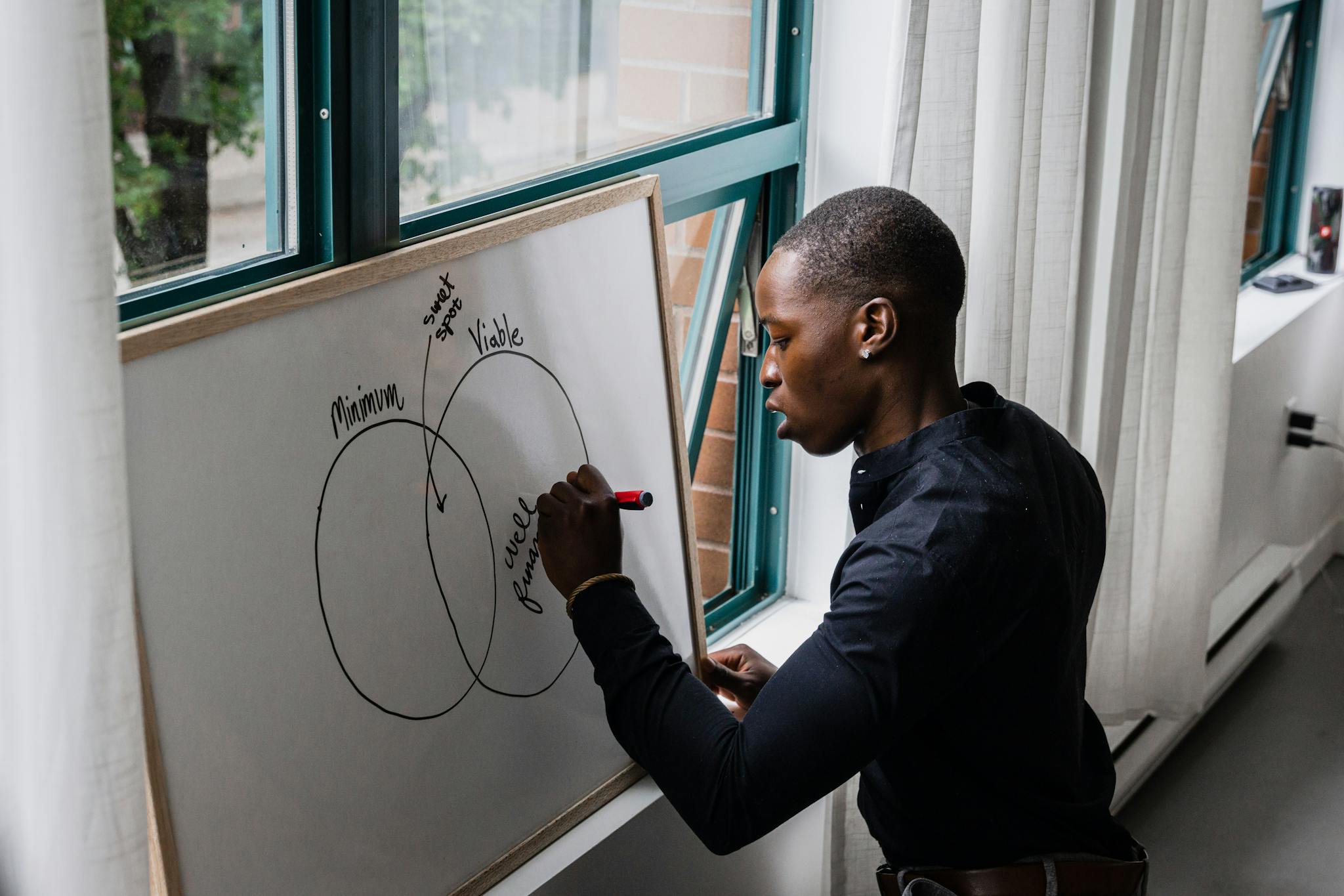 African American man writing on whiteboard with Venn diagram, indoors.